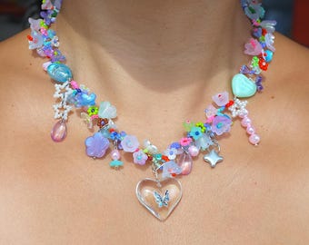 May include: A colorful beaded necklace with a variety of flowers, hearts, and stars. A clear heart charm with a silver butterfly is the centerpiece of the necklace.