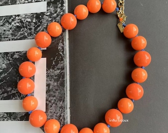 May include: A bright orange statement necklace with large round beads and a gold chain clasp. The necklace is strung on a blue cord.