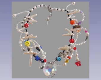 May include: A multi-strand necklace with white pearls, black beads, and colorful charms. The charms include smiley faces, stars, and seashells. A large crystal heart pendant hangs from the center of the necklace.