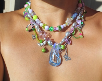 May include: A layered necklace with multiple strands of beads in various colors, including green, pink, white, and blue. The necklace features a variety of charms, including a butterfly, a flower, and a teardrop-shaped pendant.