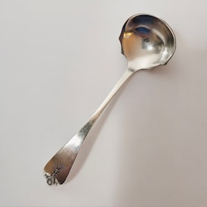 May include: A silver ladle with a decorative handle. The ladle has a rounded bowl and a long, slender handle.