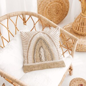 Puede incluir: Una silla de mimbre tejida con un coj&iacute;n blanco y una almohada beige con un dise&ntilde;o tejido. La silla est&aacute; en una habitaci&oacute;n con una pared blanca y una alfombra tejida.