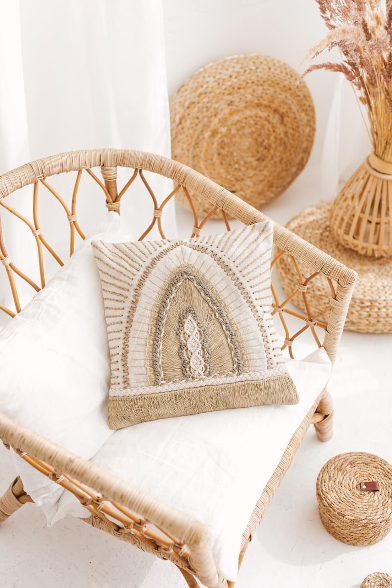 Puede incluir: Una silla de mimbre tejida con un coj&iacute;n blanco y una almohada beige con un dise&ntilde;o tejido. La silla est&aacute; en una habitaci&oacute;n con una pared blanca y una alfombra tejida.