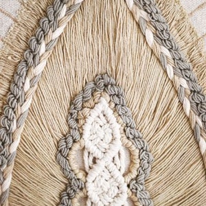 Puede incluir: Primer plano de un tapiz de macram&eacute; beige y gris con un patr&oacute;n tejido. El macram&eacute; est&aacute; hecho con fibras naturales gruesas y tiene un borde con flecos.