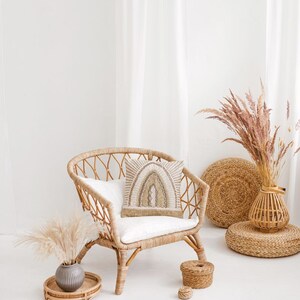 Puede incluir: Una silla de mimbre con un coj&iacute;n blanco y una almohada estampada se encuentra en una habitaci&oacute;n blanca con hierba de la pampa seca en un jarr&oacute;n de mimbre. Hay dos cestas tejidas en el suelo.