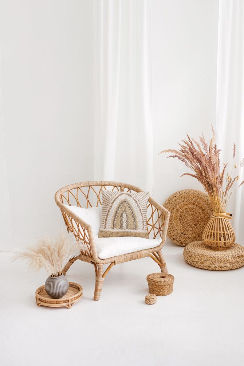 Puede incluir: Una silla de mimbre con un coj&iacute;n blanco y una almohada estampada se encuentra en una habitaci&oacute;n blanca con hierba de la pampa seca en un jarr&oacute;n de mimbre. Hay dos cestas tejidas en el suelo.