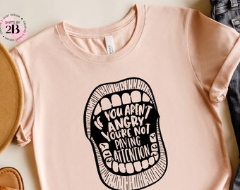 May include: A pink t-shirt with a black graphic of a mouth with the text "If you aren't angry you're not paying attention".
