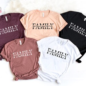 May include: Five t-shirts in different colors with the text "FAMILY" printed on the front. The text is in a bold, serif font and is stacked vertically. The names "Nick", "Emma", "Amelia", "Mia", and "Ava" are printed below the word "FAMILY" in a smaller, cursive font.