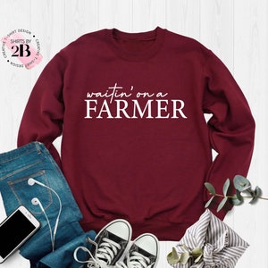 May include: A maroon sweatshirt with the text "waitin' on a FARMER" printed in white on the front.
