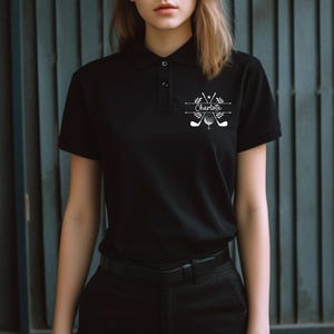 May include: Black polo shirt with a white graphic design featuring crossed golf clubs, a golf ball, and the name "Charlotte".