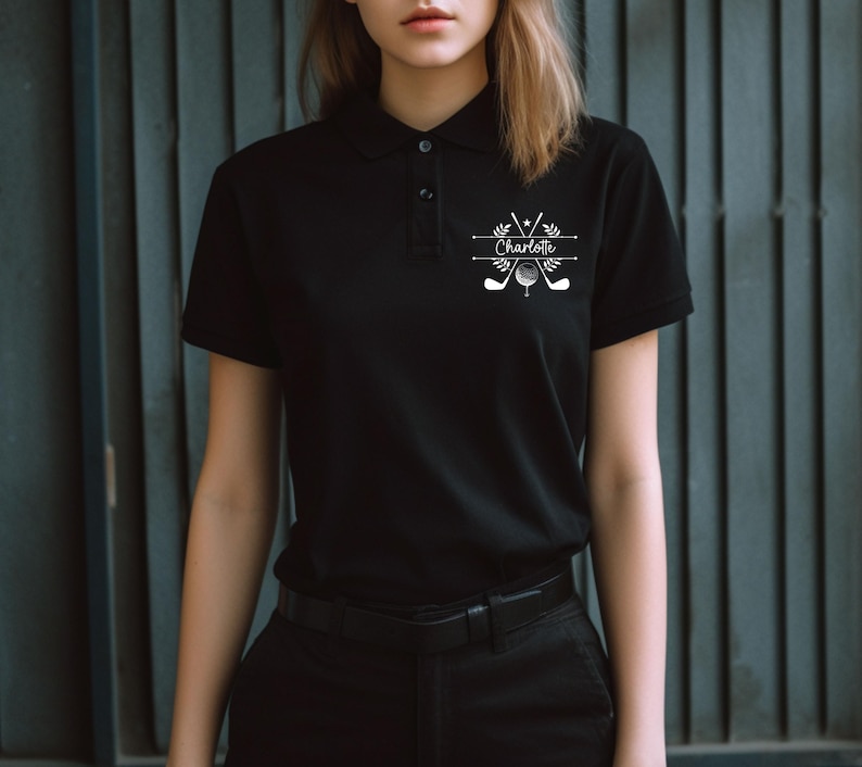 May include: Black polo shirt with a white graphic design featuring crossed golf clubs, a golf ball, and the name "Charlotte".