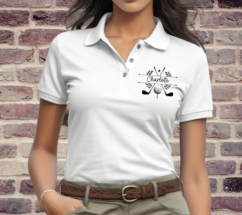 May include: White polo shirt with a black golf-themed design featuring crossed golf clubs, a golf ball, and the name "Charlotte".