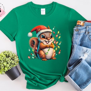 May include: A green t-shirt featuring a cartoon image of a squirrel wearing a Santa hat and holding Christmas lights.