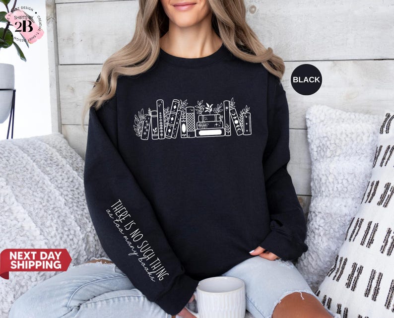 May include: Black sweatshirt featuring a white illustration of books and plants. The sleeve displays the text "THERE IS NO SUCH THING as too many books." A black circle indicates the color. The crew neck top is a casual style.