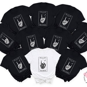 May include: A set of black t-shirts with a white graphic of a skeleton hand making a rock and roll sign. The shirts have the text "The Coven" printed on them. One white t-shirt has the text "The Bride" printed on it.