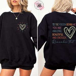 May include: Black sweatshirt with a rainbow heart on the front and the text "To the person behind me you are amazing beautiful and enough. Remember that" on the back.