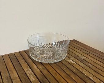 May include: A clear glass bowl with a diamond pattern on the sides. The bowl is sitting on a wooden surface.