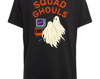 May include: Black t-shirt with the words "SQUAD GHOULS" in orange lettering. The graphic features two ghost figures, a television set, and the text "THE DRANORMAL". A remote control sits on a small table.
