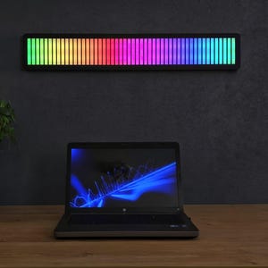 Peut inclure: Une barre lumineuse LED rectangulaire montée horizontalement, présentant un spectre vibrant de segments de couleur verticaux allant du vert et jaune au rouge, rose et bleu. L'appareil affiche un dégradé de lumière continu sur sa surface.