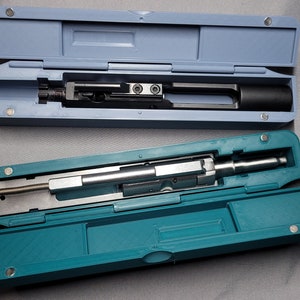May include: Two open cases with different coloured lids. The top case is light blue and contains a black metal object. The bottom case is teal and contains a silver metal object.