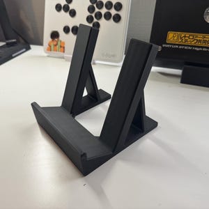 以下が含まれることがあります： アイテムを展示するための、2つの角度のついた支えが付いた黒いプラスチック製のスタンド。スタンドは3Dプリントされたプラスチック製です。