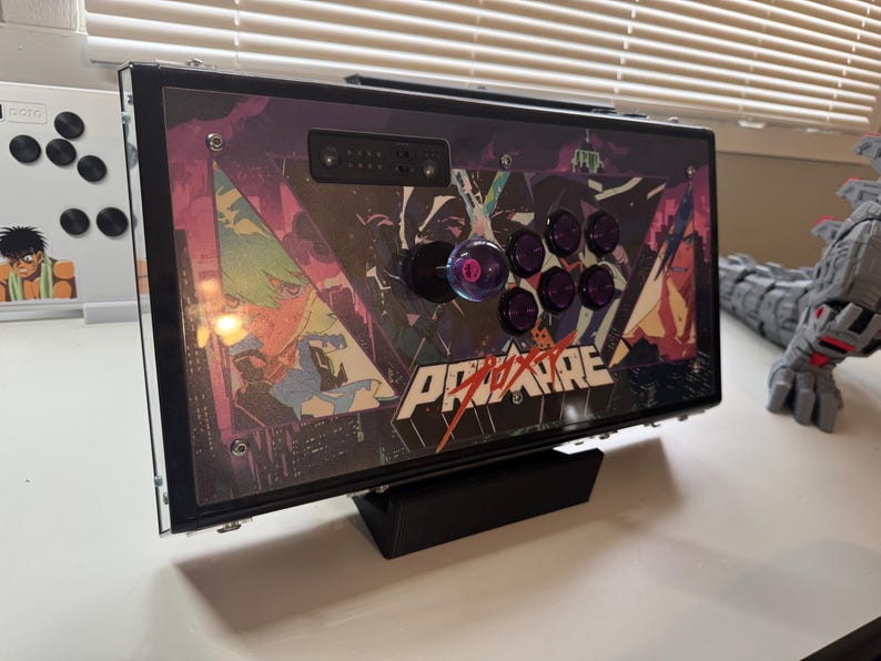 Pu&ograve; includere: Un joystick da arcade nero con un design personalizzato che presenta personaggi anime e il testo "Pro-Am". Il joystick ha otto pulsanti viola e un joystick nero e viola.