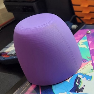 May include: A purple 3D printed cup with a smooth, rounded surface. The cup is made with a layered printing technique, visible in the subtle lines on the surface.