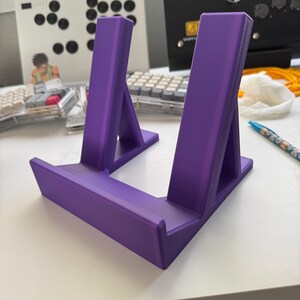 Pu&ograve; includere: Un supporto per telefono o tablet in plastica viola con due supporti inclinati. Il supporto &egrave; progettato per tenere un dispositivo in posizione verticale.