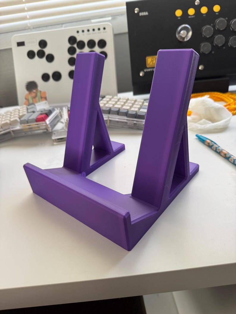 Pu&ograve; includere: Un supporto per telefono o tablet in plastica viola con due supporti inclinati. Il supporto &egrave; progettato per tenere un dispositivo in posizione verticale.