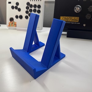 Pu&ograve; includere: Un supporto per telefono in plastica blu con due supporti inclinati. Il supporto &egrave; progettato per tenere un telefono in posizione verticale.