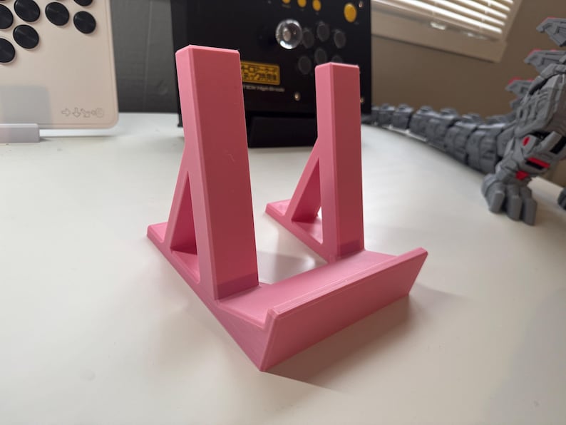 Pu&ograve; includere: Un supporto in plastica rosa con due supporti inclinati. Il supporto &egrave; progettato per tenere un piccolo oggetto, come un telefono o un tablet.