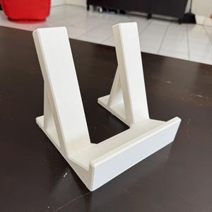 Pu&ograve; includere: Supporto in plastica bianca con due supporti inclinati per tenere un tablet o un libro.