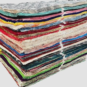 May include: A stack of handmade paper with a variety of colors, including blue, pink, yellow, and green. The edges of the paper are rough, and the stack is bound together with a white string. The paper appears to be of high quality.