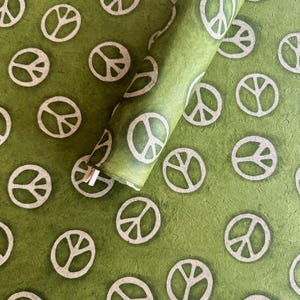 May include: Green wrapping paper with a repeating pattern of white peace symbols. A roll of the paper is partially unrolled, revealing the pattern. The paper has a textured appearance.