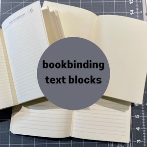 May include: Multiple off-white bookbinding text blocks with cream-colored paper pages. Some pages feature horizontal lines and the printed text "luglio-july-juillet-juli 09" at the top. The paper is arranged in open stacks, showcasing the internal structure.