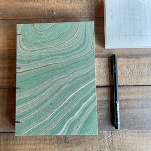 May include: A green journal with a marbled cover. The cover has white and gold lines.