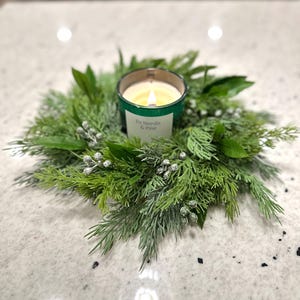 May include: A green candle with a frosted glass jar and a white label that reads "Fir Needle & Pine" is surrounded by a green wreath with white berries.