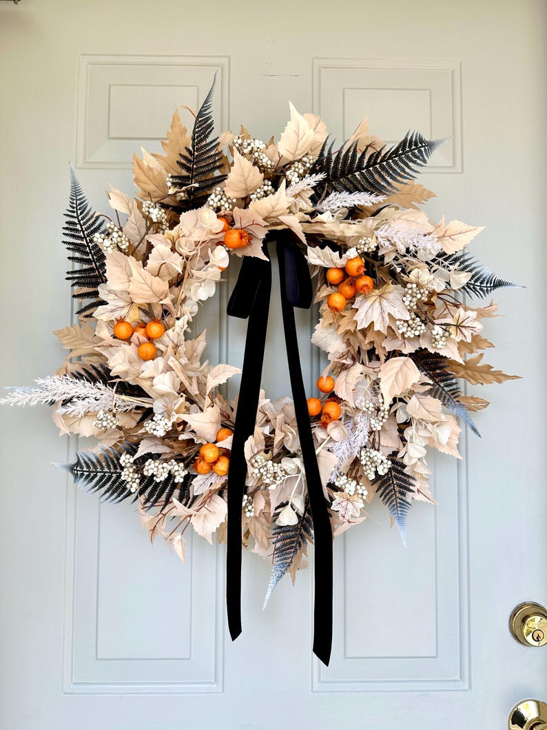 May include: A fall wreath with beige and white leaves, orange berries, and black velvet ribbon.