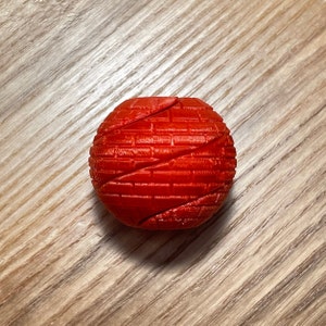 May include: A red 3D printed ball with a textured surface. The ball is made up of multiple interlocking pieces.