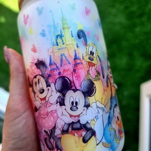 May include: White ceramic tumbler with a colourful watercolour design featuring Mickey Mouse, Minnie Mouse, Goofy, Donald Duck, and Pluto in front of Cinderella's Castle. The tumbler has a wooden lid.