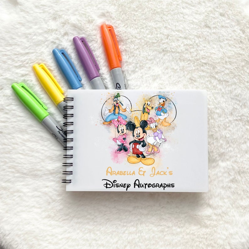 May include: A white spiral bound notebook with a colorful illustration of Mickey Mouse and friends. The notebook has the text "Arabella & Jack's Disney Autographs" printed on the front.