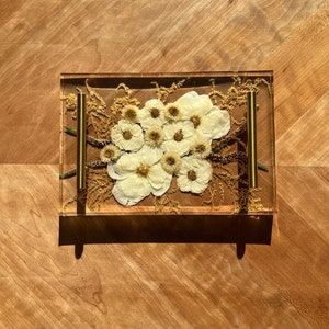 May include: A rectangular tray made of clear resin with gold metal handles. The tray is filled with dried white flowers and greenery.
