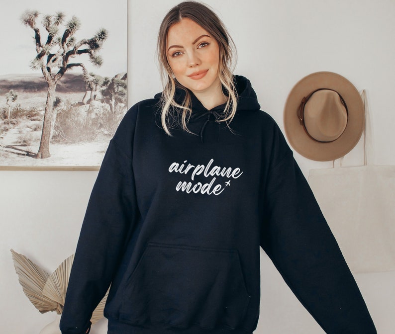 May include: A black hooded sweatshirt with the words "airplane mode" in white script. The sweatshirt has a front pocket and a drawstring hood. The model is wearing the sweatshirt.