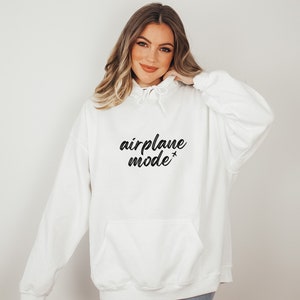 May include: White hoodie with a front pocket and drawstring hood. The phrase "airplane mode" is printed in black script across the chest, with a small airplane graphic. A casual, comfortable sweatshirt.