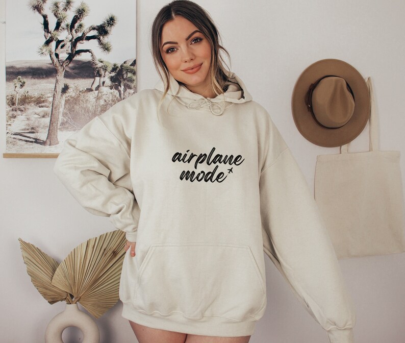 May include: Cream-colored hoodie with the text "airplane mode" in black script. The hoodie has a drawstring hood and a front pocket. A casual, comfortable garment for everyday wear.