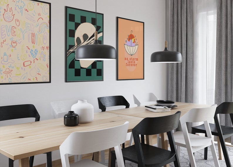Puede incluir: Un comedor con una mesa de madera clara, sillas negras y blancas, dos l&aacute;mparas colgantes negras y tres cuadros en la pared. Una l&aacute;mina muestra el texto "no storm lasts forever" con una ilustraci&oacute;n gr&aacute;fica de un paraguas y un sol.