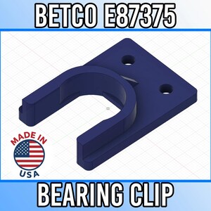 Puede incluir: Un clip de rodamiento azul marino con un diseño en forma de U, fijado a una base rectangular con dos agujeros. Se muestra el texto "BETCO E87375" y "BEARING CLIP". Incluye un emblema "MADE IN USA".