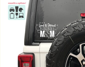 May include: White vinyl decal applied to a vehicle window. The decal reads "Loud & Proud BASEBALL MOM" with a baseball graphic. Additional icons are visible in the upper left corner.