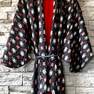May include: A black kimono robe featuring a repeating white and red geometric pattern. The garment has wide sleeves, an open front design, and a solid red interior lining. A thin, dark blue cord is tied around the waist to secure the front panels.