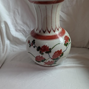 May include: A ceramic vase with a bulbous base and a flared neck. The vase is off-white with red detailing and a floral pattern of red flowers and green leaves. It has a crackle glaze finish.